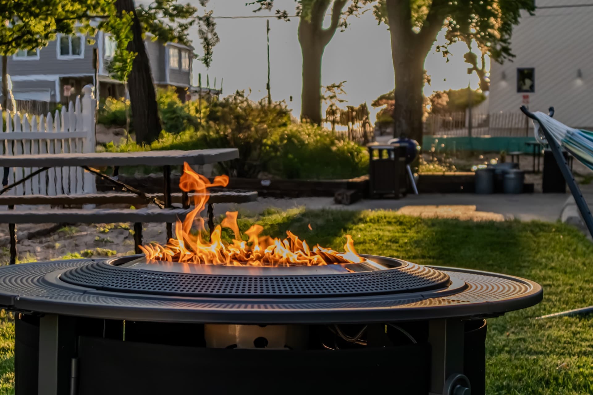Firepit glowing on the lawn behind Silver Beach Inn at golden hour, with a hammock strung beside it