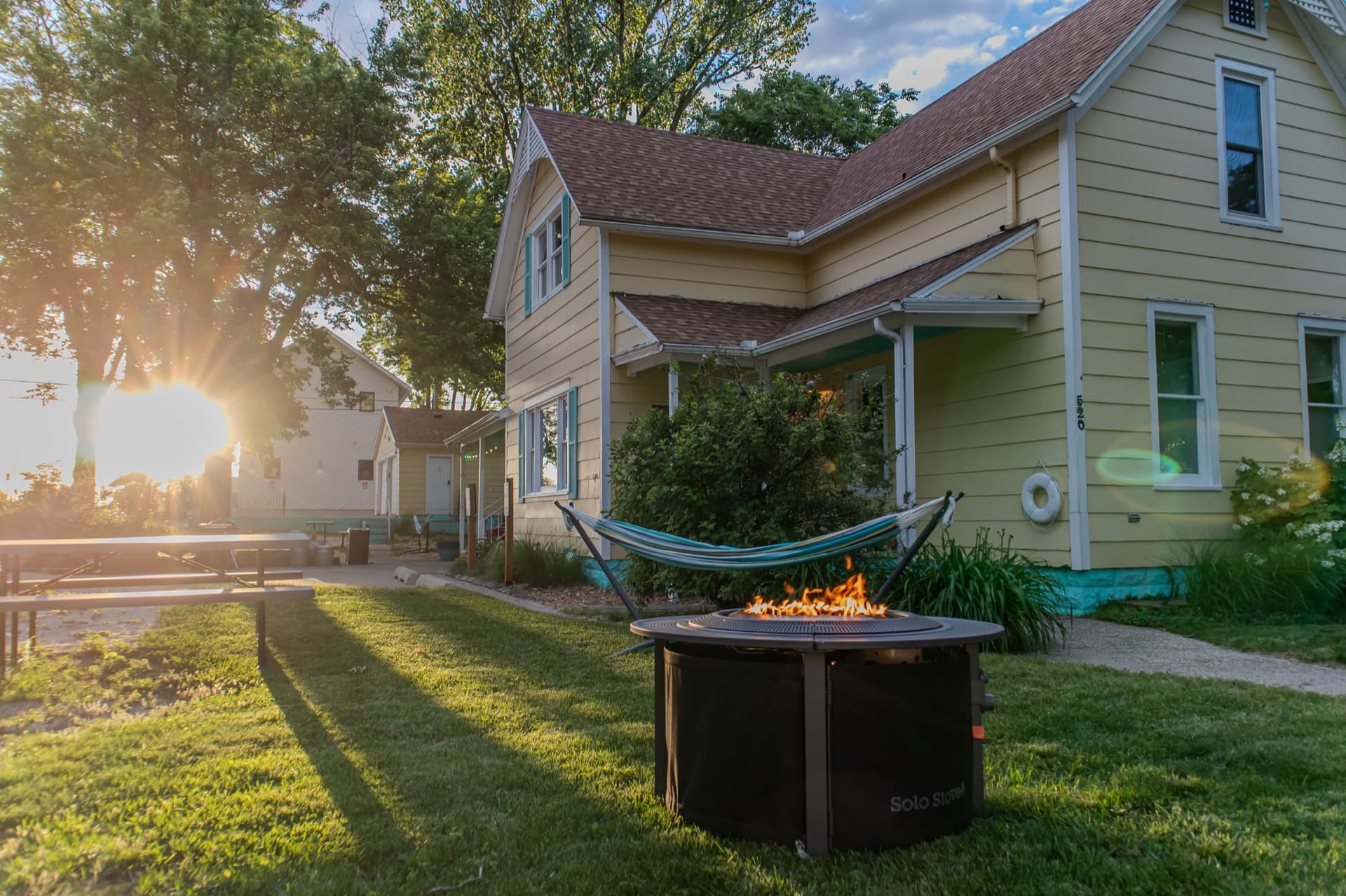 Golden-hour light through the trees behind Silver Beach Inn, with a lit firepit and hammock on the lawn
